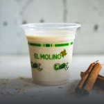 Vaso transparente con avena fría tradicional y un toque de canela, destacando el logo verde de Panadería El Molino, acompañado de astillas de canela en Cali.