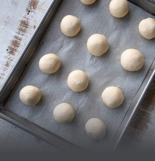 Bolitas de Pandebono para Hornear - Panadería El Molino Cali Bandeja metálica con bolitas de masa cruda de pandebono preparadas y listas para hornear en casa, de Panadería El Molino, Cali.