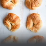 Varios cachitos de hojaldre recién horneados sobre una tabla de madera, típicos de Panadería El Molino en Cali.