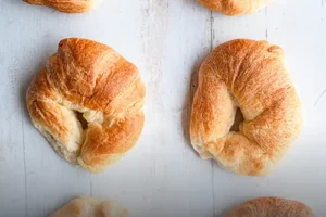 Varios cachitos de hojaldre recién horneados sobre una tabla de madera, típicos de Panadería El Molino en Cali.