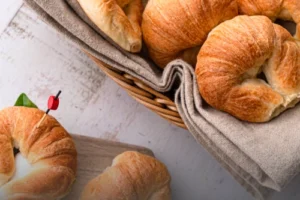 Cachos de pan artesanales dorados en una canasta de mimbre y un sándwich de cacho preparado con espinaca sobre una mesa de madera clara en Panadería El Molino.