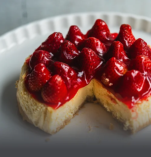Torta de cheesecake cremosa con cobertura de mermelada de frutos rojos, fresas y arándanos frescos sobre una base de galleta en Panadería El Molino.