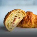 Croissant artesanal relleno de jamón y queso derretido, con corteza de hojaldre dorada sobre una superficie de madera en Panadería El Molino, Cali.