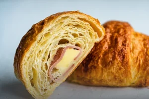 Croissant artesanal relleno de jamón y queso derretido, con corteza de hojaldre dorada sobre una superficie de madera en Panadería El Molino, Cali.