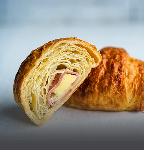 Croissant artesanal relleno de jamón y queso derretido, con corteza de hojaldre dorada sobre una superficie de madera en Panadería El Molino, Cali.