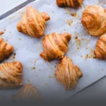 Bandeja con croissants artesanales recién horneados, crujientes y dorados, sobre papel mantequilla en una panadería de Cali.