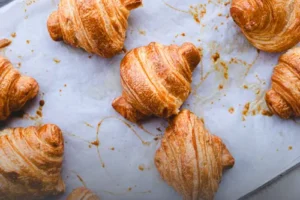Bandeja con croissants artesanales recién horneados, crujientes y dorados, sobre papel mantequilla en una panadería de Cali.