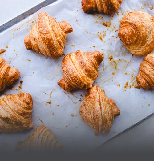 Bandeja con croissants artesanales recién horneados, crujientes y dorados, sobre papel mantequilla en una panadería de Cali.