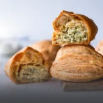Empanada de pollo artesanal con masa dorada y crujiente, partida a la mitad mostrando su relleno de pollo desmechado sobre una tabla de madera en Panadería El Molino.