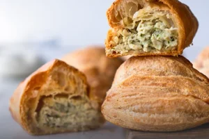 Empanada de pollo artesanal con masa dorada y crujiente, partida a la mitad mostrando su relleno de pollo desmechado sobre una tabla de madera en Panadería El Molino.