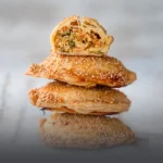 Empanada de pollo artesanal con masa dorada y crujiente, partida a la mitad mostrando su relleno de pollo desmechado sobre una tabla de madera en Panadería El Molino.