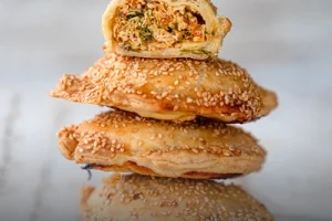 Empanada de pollo artesanal con masa dorada y crujiente, partida a la mitad mostrando su relleno de pollo desmechado sobre una tabla de madera en Panadería El Molino.