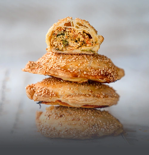 Empanada de pollo artesanal con masa dorada y crujiente, partida a la mitad mostrando su relleno de pollo desmechado sobre una tabla de madera en Panadería El Molino.