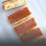 Milhoja artesanal de varias capas de hojaldre crujiente rellenas de arequipe y cubiertas con azúcar glass, servida en un plato de Panadería El Molino en Cali.