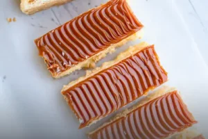 Milhoja artesanal de varias capas de hojaldre crujiente rellenas de arequipe y cubiertas con azúcar glass, servida en un plato de Panadería El Molino en Cali.