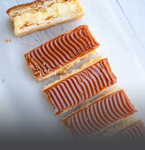 Milhoja artesanal de varias capas de hojaldre crujiente rellenas de arequipe y cubiertas con azúcar glass, servida en un plato de Panadería El Molino en Cali.