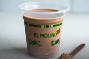 Vaso de Milo frío con la marca de Panadería El Molino, acompañado por una cuchara de madera con polvo de chocolate, en Cali.