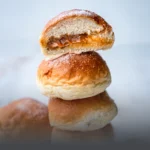 Varios mojicones de arequipe (pan dulce colombiano) recién horneados, suaves y esponjosos con una generosa cobertura de dulce de leche, sobre una tabla de madera rústica en Panadería El Molino, Cali.