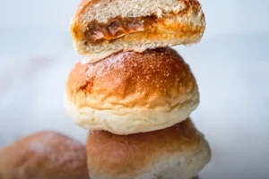 Varios mojicones de arequipe (pan dulce colombiano) recién horneados, suaves y esponjosos con una generosa cobertura de dulce de leche, sobre una tabla de madera rústica en Panadería El Molino, Cali.