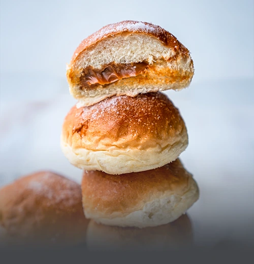 Varios mojicones de arequipe (pan dulce colombiano) recién horneados, suaves y esponjosos con una generosa cobertura de dulce de leche, sobre una tabla de madera rústica en Panadería El Molino, Cali.