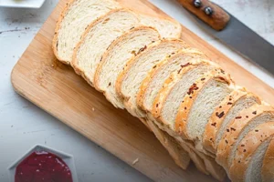 Vista superior de pan aliñado especial tajado sobre una tabla de madera, acompañado de mantequilla y mermelada en la Panadería El Molino de Cali.
