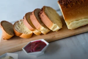 Pan aliñado de mantequilla tajado sobre una tabla de madera, acompañado de mermelada de frutos rojos y mantequilla en la mesa de Panadería El Molino.