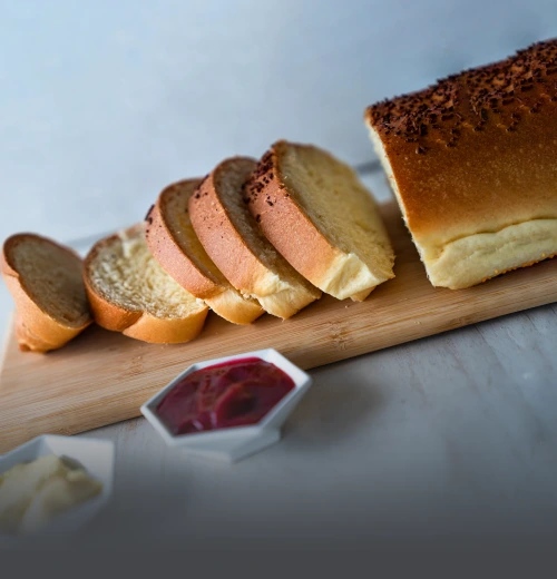 Pan aliñado de mantequilla tajado sobre una tabla de madera, acompañado de mermelada de frutos rojos y mantequilla en la mesa de Panadería El Molino.