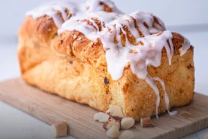 Pan danés artesanal con glaseado brillante y abundante cobertura de nueces picadas sobre una superficie de madera rústica en Panadería El Molino, Cali.
