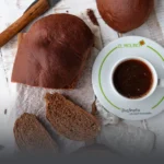 Hogaza de pan de chocolate artesanal rebanado, mostrando su miga suave y oscura, servido junto a un café en Panadería El Molino, Cali.
