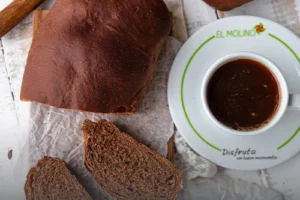 Hogaza de pan de chocolate artesanal rebanado, mostrando su miga suave y oscura, servido junto a un café en Panadería El Molino, Cali.