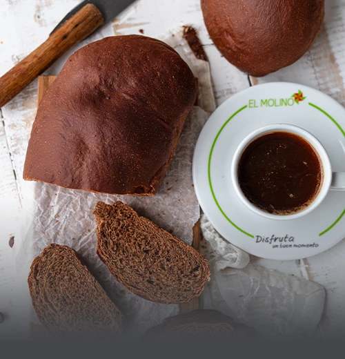 Hogaza de pan de chocolate artesanal rebanado, mostrando su miga suave y oscura, servido junto a un café en Panadería El Molino, Cali.