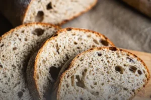 Rebanadas de pan francés de campo con corteza tostada y miga con alvéolos grandes sobre una tabla de madera rústica en Panadería El Molino, Cali.