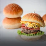 Pan de hamburguesa artesanal suave con semillas de ajonjolí, junto a una hamburguesa gourmet recién preparada en Cali.