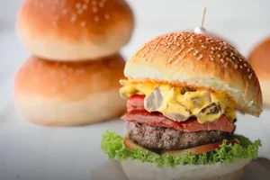 Pan de hamburguesa artesanal suave con semillas de ajonjolí, junto a una hamburguesa gourmet recién preparada en Cali.