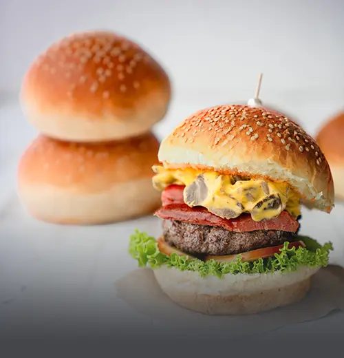 Pan de hamburguesa artesanal suave con semillas de ajonjolí, junto a una hamburguesa gourmet recién preparada en Cali.
