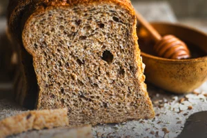 Tajadas de pan integral artesanal 11 granos multicereal, mostrando la miga densa con semillas, sobre una tabla de madera rústica en Panadería El Molino.