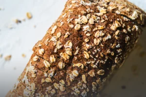 Pan integral artesanal de 6 granos con corteza cubierta de semillas, tajado sobre una mesa de madera rústica en Panadería El Molino, Cali.