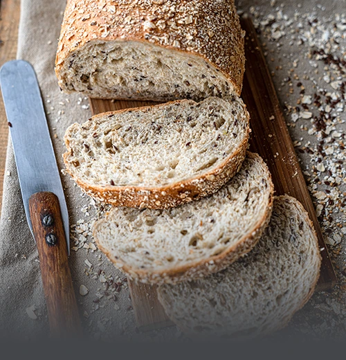 Pan Integral Multicereal Rebanado - Panadería El Molino Cali Hogaza de pan integral multicereal artesanal rebanado, mostrando su miga rica en semillas y cubierta de avena, elaborado en Panadería El Molino, Cali.