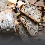 Pan de masa madre sourdough con arándanos y nueces tajado sobre una tabla de madera, con frutos secos esparcidos alrededor en Panadería El Molino, Cali.