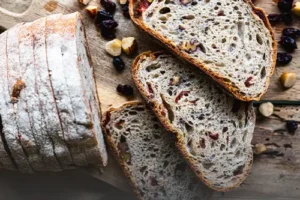 Pan de masa madre sourdough con arándanos y nueces tajado sobre una tabla de madera, con frutos secos esparcidos alrededor en Panadería El Molino, Cali.