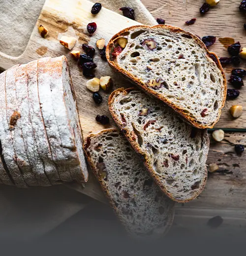 Pan de masa madre sourdough con arándanos y nueces tajado sobre una tabla de madera, con frutos secos esparcidos alrededor en Panadería El Molino, Cali.