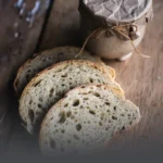 Rebanadas de pan de masa madre sourdough sobre mesa de madera rústica junto a un frasco artesanal envuelto en papel en Panadería El Molino, Cali.