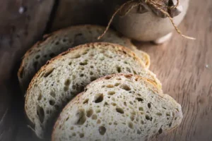 Rebanadas de pan de masa madre sourdough sobre mesa de madera rústica junto a un frasco artesanal envuelto en papel en Panadería El Molino, Cali.