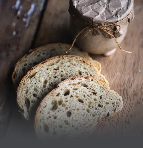 Rebanadas de pan de masa madre sourdough sobre mesa de madera rústica junto a un frasco artesanal envuelto en papel en Panadería El Molino, Cali.