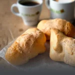 Tres pandeyucas tradicionales recién horneados, con textura crujiente y dorada, acompañados de dos tazas de café con el logo de Panadería El Molino al fondo, en Cali.