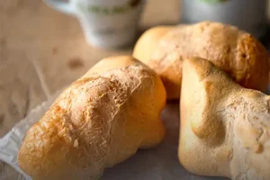 Tres pandeyucas tradicionales recién horneados, con textura crujiente y dorada, acompañados de dos tazas de café con el logo de Panadería El Molino al fondo, en Cali.