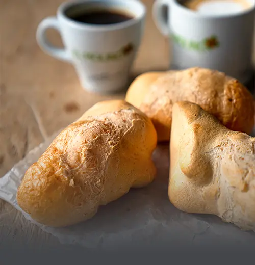 Tres pandeyucas tradicionales recién horneados, con textura crujiente y dorada, acompañados de dos tazas de café con el logo de Panadería El Molino al fondo, en Cali.