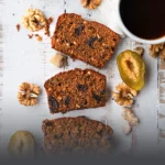 Tres porciones de cake negro artesanal con frutos secos, nueces y ciruelas, servidas sobre una mesa rústica junto a una taza de café, en Panadería El Molino, Cali.