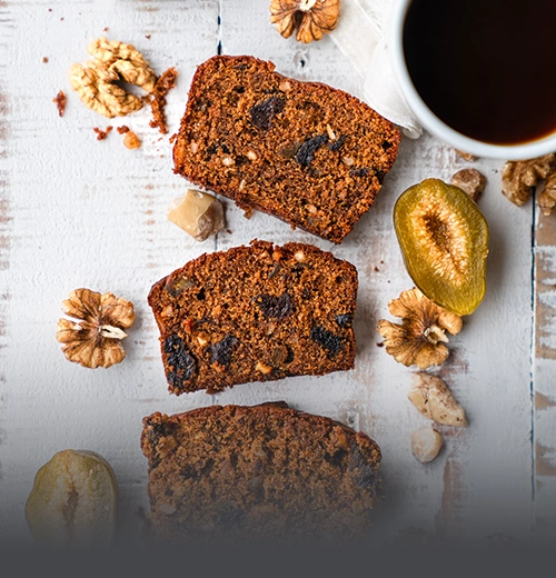 Porción de Cake Negro Artesanal - Panadería El Molino Cali Tres porciones de cake negro artesanal con frutos secos, nueces y ciruelas, servidas sobre una mesa rústica junto a una taza de café, en Panadería El Molino, Cali.