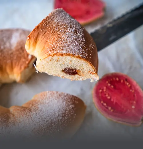 Porción de roscón de guayaba artesanal espolvoreado con azúcar, mostrando el relleno de dulce de guayaba, con frutas frescas de guayaba al fondo en Panadería El Molino.